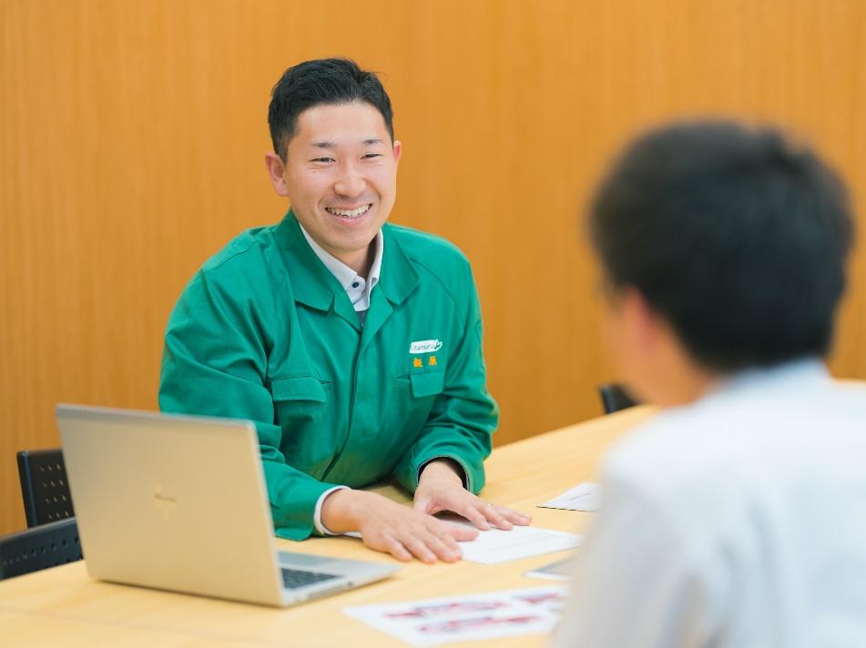 株式会社北村製作所で、ノートパソコンを前に打ち合わせを行う緑色の作業着姿の男性社員。