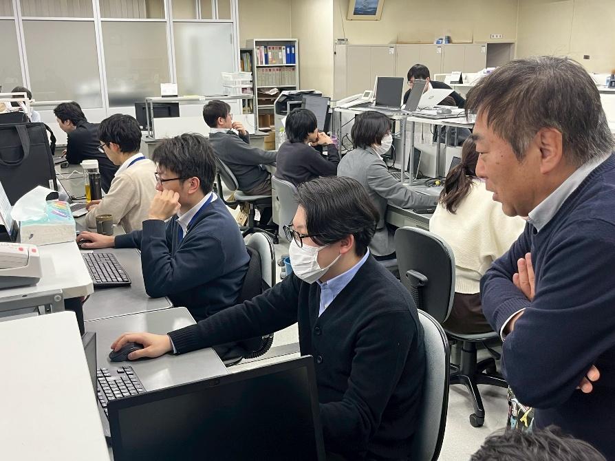 JCCソフト株式会社の新潟支社や上越本社にて、真剣な表情でシステム開発に取り組むエンジニアたちの業務風景。若手社員がベテランの指導を受けつつ、建設業や製造業のDXを支えるオーダーメイドのソフトウェア開発に邁進。人間力と技術力を磨き、地域社会の豊かさに貢献する。